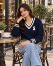 Woman wearing dark blue varsity cable knit V-neck sweater by Purple Imli in a city street look
