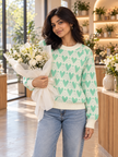 Woman wearing green heart jacquard sweater by Purple Imli in a city street look